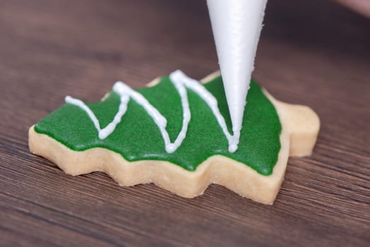 Close up of drawing gingerbread Christmas tree sugar cookie on wooden table background with green icing, concept of holiday celebration.