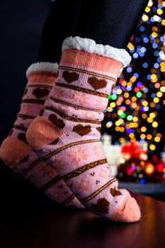 Female legs in Christmas colorful socks near Christmas tree.