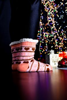 Female legs in Christmas colorful socks near Christmas tree.