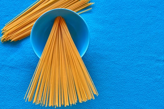 Some uncooked spaghetti in bowl with blue background