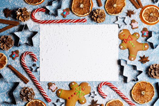 Christmas flat lay background with traditional gingerbread cookies dried orange candy canes on blue, card with copy space for text