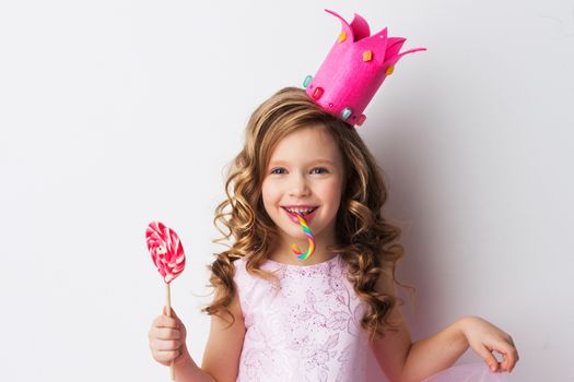 Happy laughing princess girl in crown and pink dress with lollipop and candy cane on white background