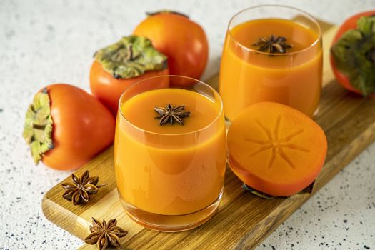 Two glasses of fresh healthy persimmon smoothie with anise stars on cutting wooden board, gray concrete background, selective focus, copy space.