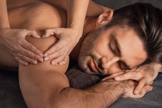 A good-looking man getting a back massage lying down at spa, Woman hand making sign heart love concept