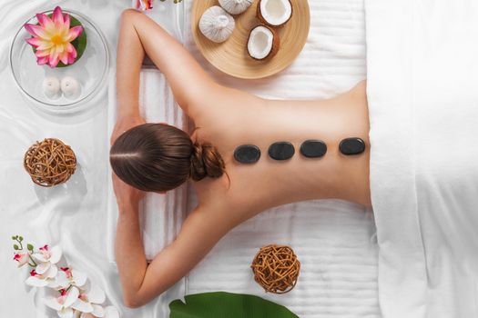 Spa stone massage, beautiful woman getting hot stones massage, beauty treatments concept. Top view. Orchid and lotus flowers coconut and herb pouches