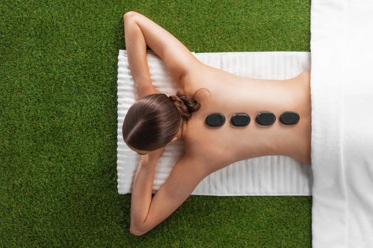 Natural body care concept, woman at spa massage with hot stones lying on grass, top view