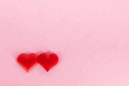 Valentine's day two red silk hearts on pink paper background, love concept