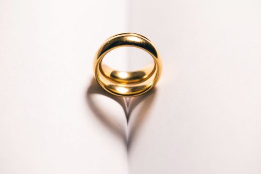 Two golden wedding ring on blank book pages background with copy space for text, heart shape shadow love concept