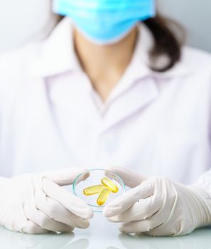 Close up Scientist hands putting in nitrile latex gloves holding Omega 3 capsule in labcoat doing experiments in lab