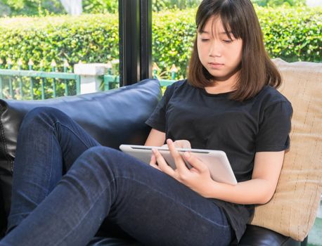 Young girl studying online from digital tablet on the sofai n living room at home