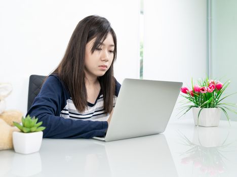 Young female student sitting in living room using laptop at desk learning online