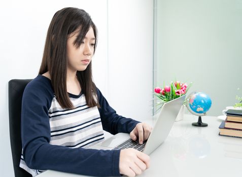 Young female student sitting in living room using laptop at desk learning online