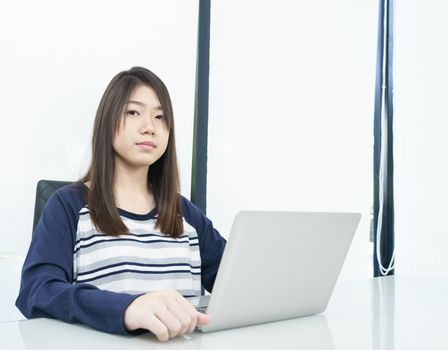 Young female student sitting in living room using laptop at desk learning online