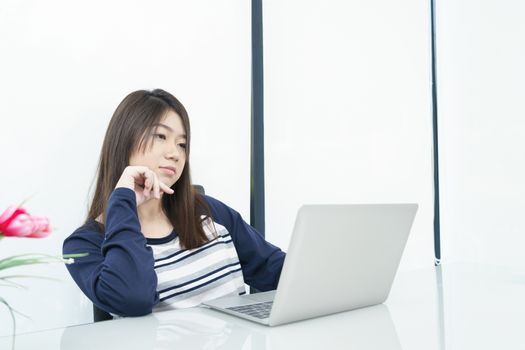 Young female student sitting in living room using laptop at desk learning online