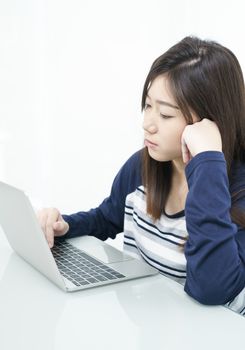 Young female student sitting in living room using laptop at desk learning online
