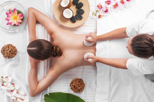 Woman at spa thai massage tow view, beauty treatments concept. Orchid and lotus flowers coconut stones and herb pouches