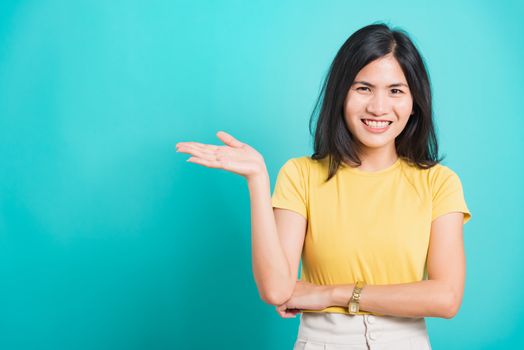 Portrait Asian beautiful young woman standing wear yellow t-shirt, She showing hand to presenting product and looking at the camera, shoot photo in a studio on a blue background, There was copy space