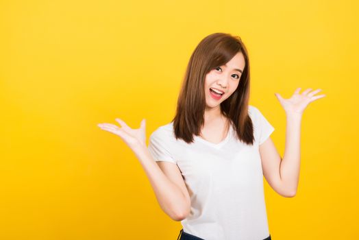 Asian happy portrait beautiful cute young woman teen standing wear t-shirt Surprised excited screaming open mouth show hand looking to camera isolated, studio shot on yellow background with copy space
