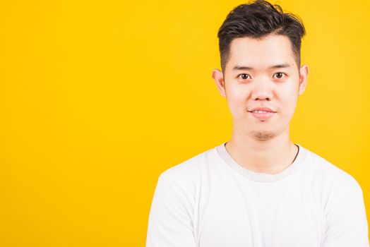 Close up portrait happy Asian handsome young man smiling standing wearing white t-shirt looking to camera, studio shot isolated yellow background