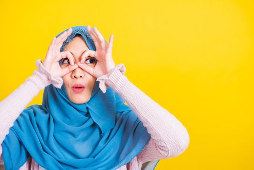 Asian Muslim Arab, Portrait of happy beautiful young woman Islam religious wear veil hijab funny smile she show gesture fingers in okay gesture symbol, OK sign over her eyes isolated yellow background