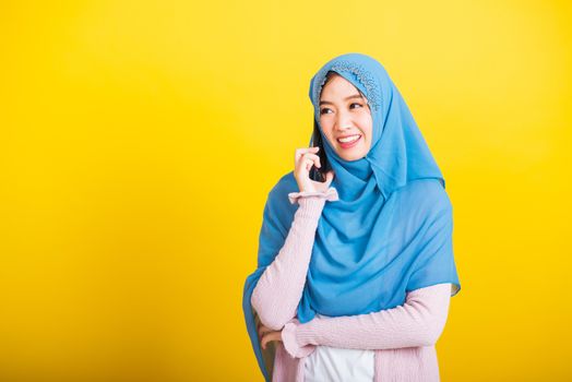 Asian Muslim Arab, Portrait of happy beautiful young woman Islam religious wear veil hijab funny smile she talking on mobile smart phone against, studio shot isolated on yellow background