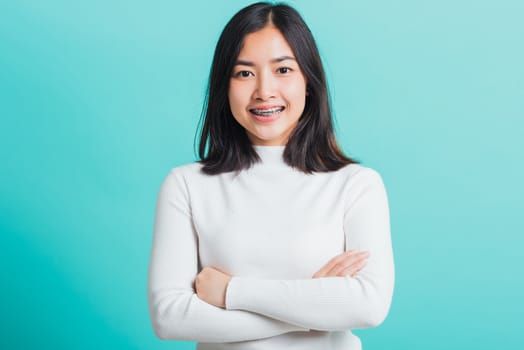 Young beautiful Asian woman smiling with crossed arms, Portrait of positive confident female stand cross one's arm, studio shot isolated on a blue background