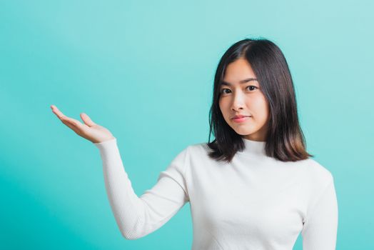 Young beautiful Asian woman smiling makeup showing product on blank hand, Portrait female demonstrate presenting something on hand, studio shot isolated on a blue background