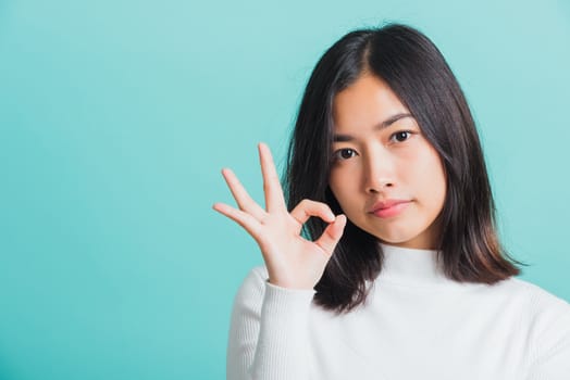 Young beautiful Asian woman smiling and showing hand the OK sign, Portrait female show finger okay gesture, studio shot isolated on a blue background