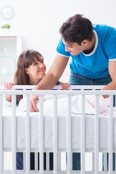 Happy young family at baby bed cot