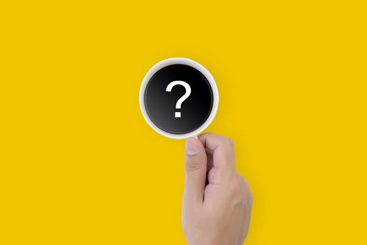 Hand holding cup of hot coffee with question mark isolated on yellow background, top view, q & a, faq or assistance for incentive, beverage or breakfast, communication and idea concept.