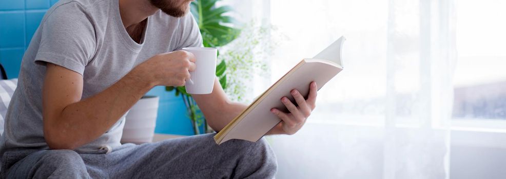 Young man reading a book sitting on sofa for rest is hobby in living room, stay home for leisure, lifestyle of new normal for social distracting, male learn and study in interesting in spare time.