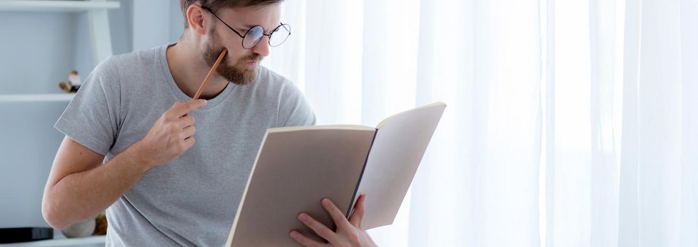 Young man reading book preparing exam at room, male learning and homework, erudition and clever, intelligent with cognition for study, knowledge and wisdom, education and lifestyle concept.