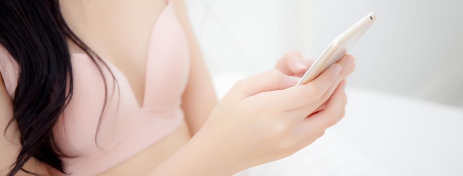 Closeup beautiful young asian woman sexy in underwear chatting on mobile phone in the bedroom, girl looking social media on smartphone for relax, communication and lifestyle concept, banner website.