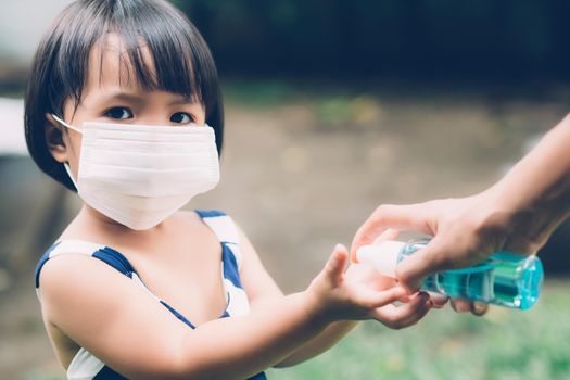 Mother take care daughter with face mask and sanitizer for protection disease flu or covid-19 outdoors, mom and child wearing medical mask clean hand for safety for outbreak of pandemic in public.