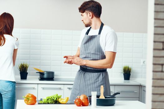 chef in an apron in the kitchen with fresh vegetables and a woman in jeans in the background