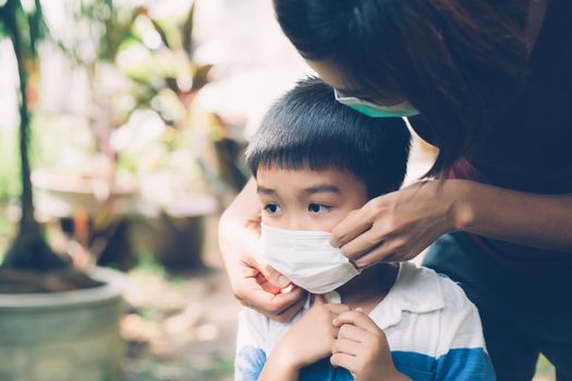 Mother take care son with face mask for protection disease flu or covid-19 outdoors, mom wearing on medical mask with child safety for protect outbreak of pandemic in public, medical concept.