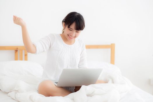 Beautiful of portrait asian young woman sitting relax and leisure with laptop computer internet online on bed in bedroom, cheerful of asia girl with gesture glad and success, lifestyle concept.