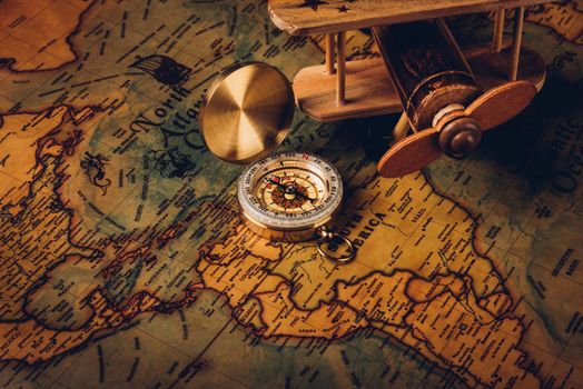 Old compass discovery and wooden plane on vintage paper antique world map