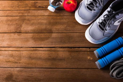 pair sports shoes, bottle water, apple and jump rope on wood table