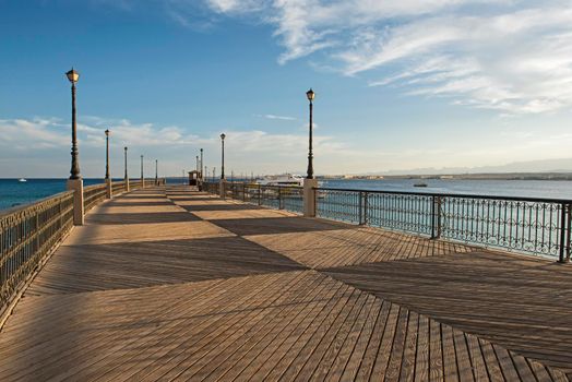 Scenic view down a large wooden jetty pier over sea in tropical coastal seaside resort