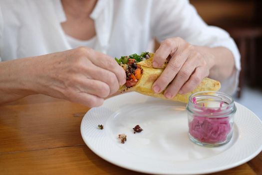 hand holding vegan wrap with quinoa, black bean, mango, cashew nut, bell pepper