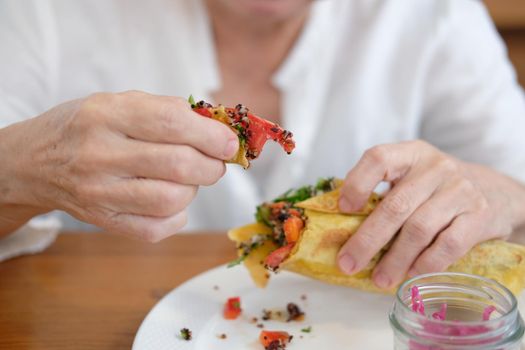 hand holding vegan wrap with quinoa, black bean, mango, cashew nut, bell pepper