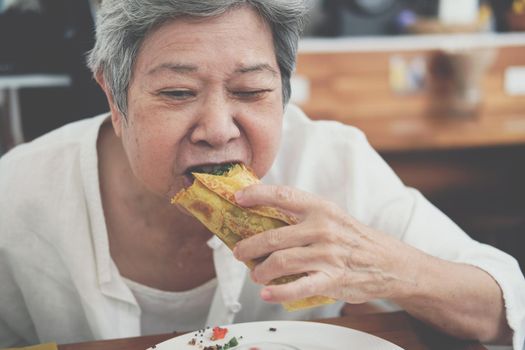 old asian elderly senior elder woman eating vegan wrap with quinoa, black bean, mango, cashew nut, bell pepper