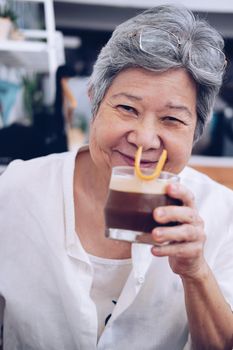 old asian elderly senior elder woman drinking iced coffee with orange syrup