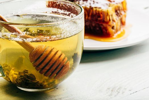 Honey dipper in cup of green tea with honeycomb on background