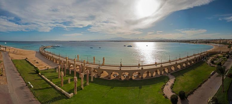 Aerial panoramic view across a beautiful landscaped garden to the sea in tropical resort with large bridge and archways on beach