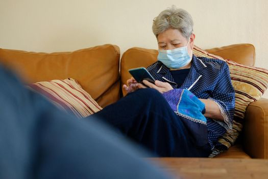 asian elder senior woman elderly wearing facial mask using mobile smart phone cellphone. mature retirement lifestyle