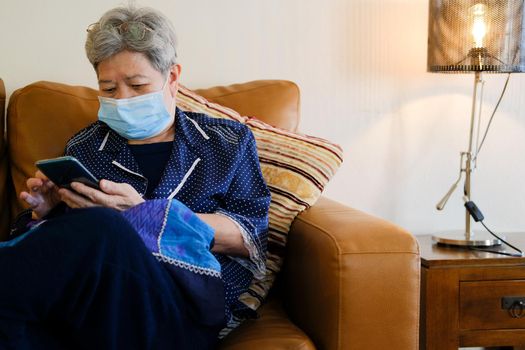 asian elder senior woman elderly wearing facial mask using mobile smart phone cellphone. mature retirement lifestyle