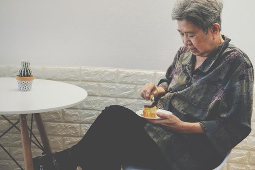 old asian elderly senior elder woman eating cheesecake at restaurant. mature retirement lifestyle