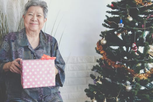 asian old elder woman elderly senior female holding gift present box near christmas tree